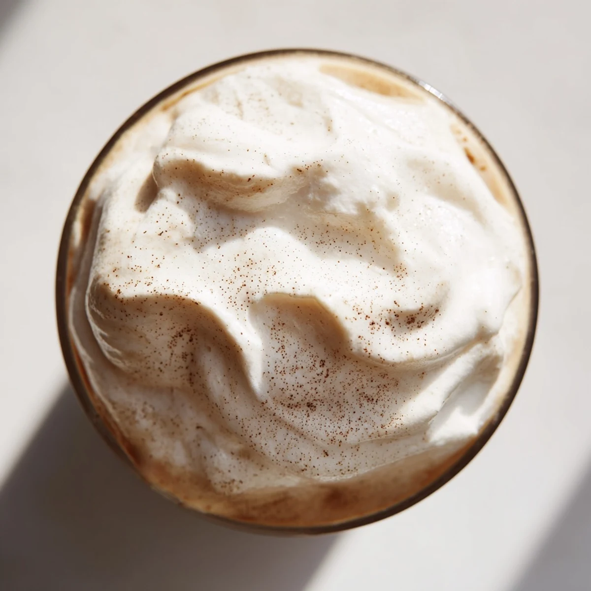 Creamy whipped Dalgona coffee floats atop a glass of cold milk, creating a striking layered effect for a café-style treat.