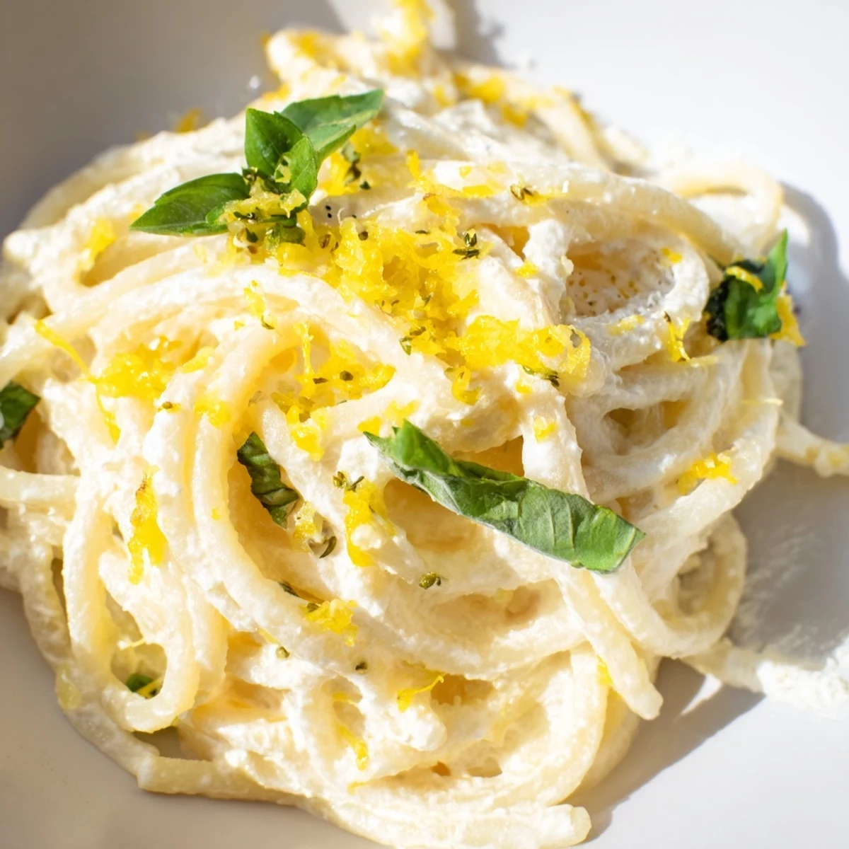 In a white ceramic bowl, creamy Lemon Ricotta Pasta is twirled with a fork, flecked with fresh basil and lemon zest.