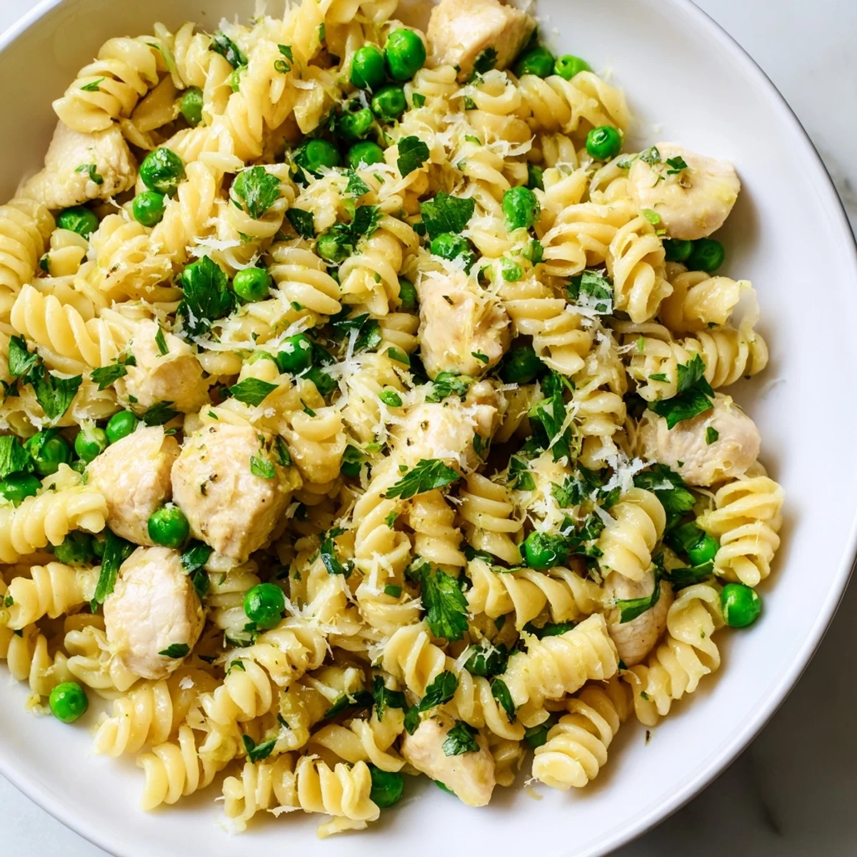 Garlic Butter Chicken & Pea Pasta features golden chicken pieces and bright green peas tossed with curly pasta in a glossy butter sauce.