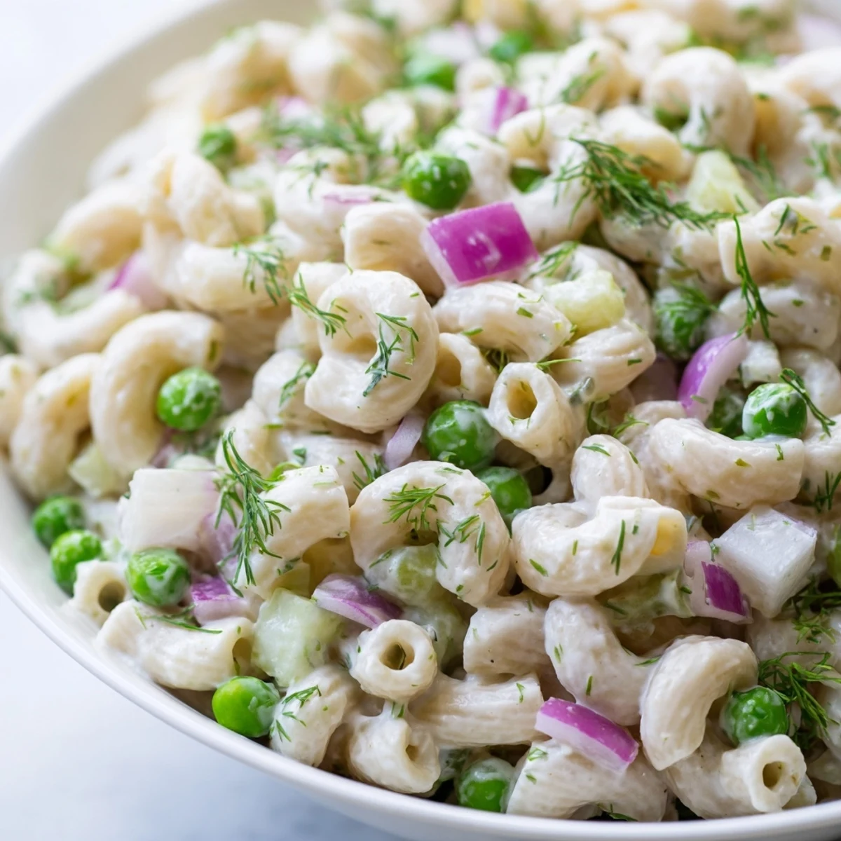 A vibrant bowl of creamy dill pickle pasta salad, featuring ditalini, peas, and diced pickles, served chilled for a picnic.