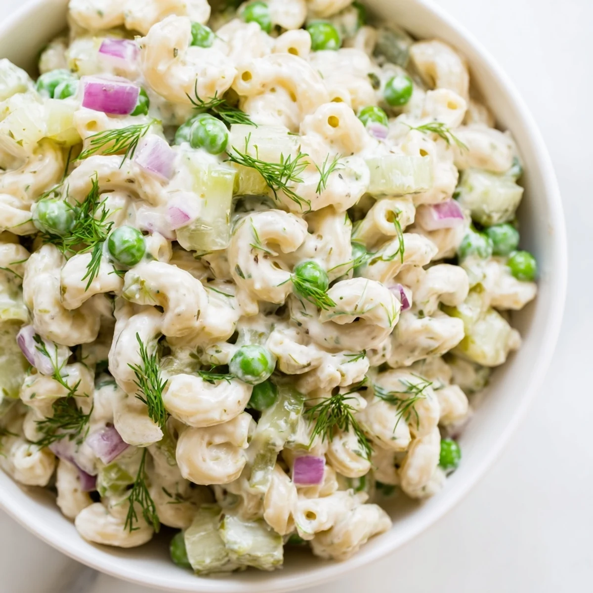 Close-up view of creamy dill pickle pasta salad, highlighting the crunchy celery, red onion, and fresh dill garnish.