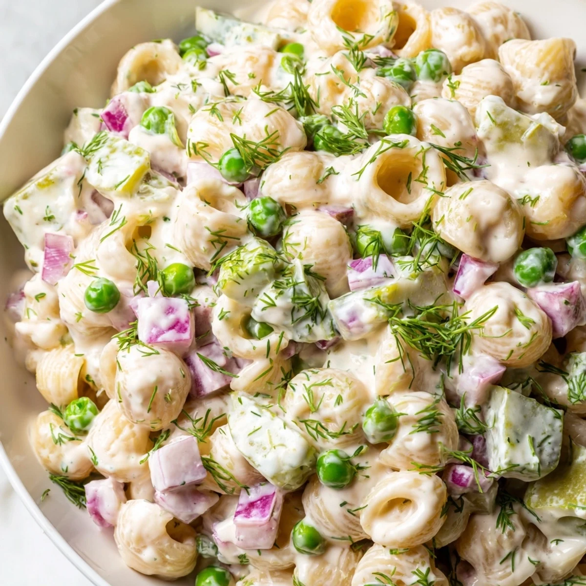 A refreshing side dish of creamy dill pickle pasta salad, perfect for potlucks and served in a white ceramic bowl.
