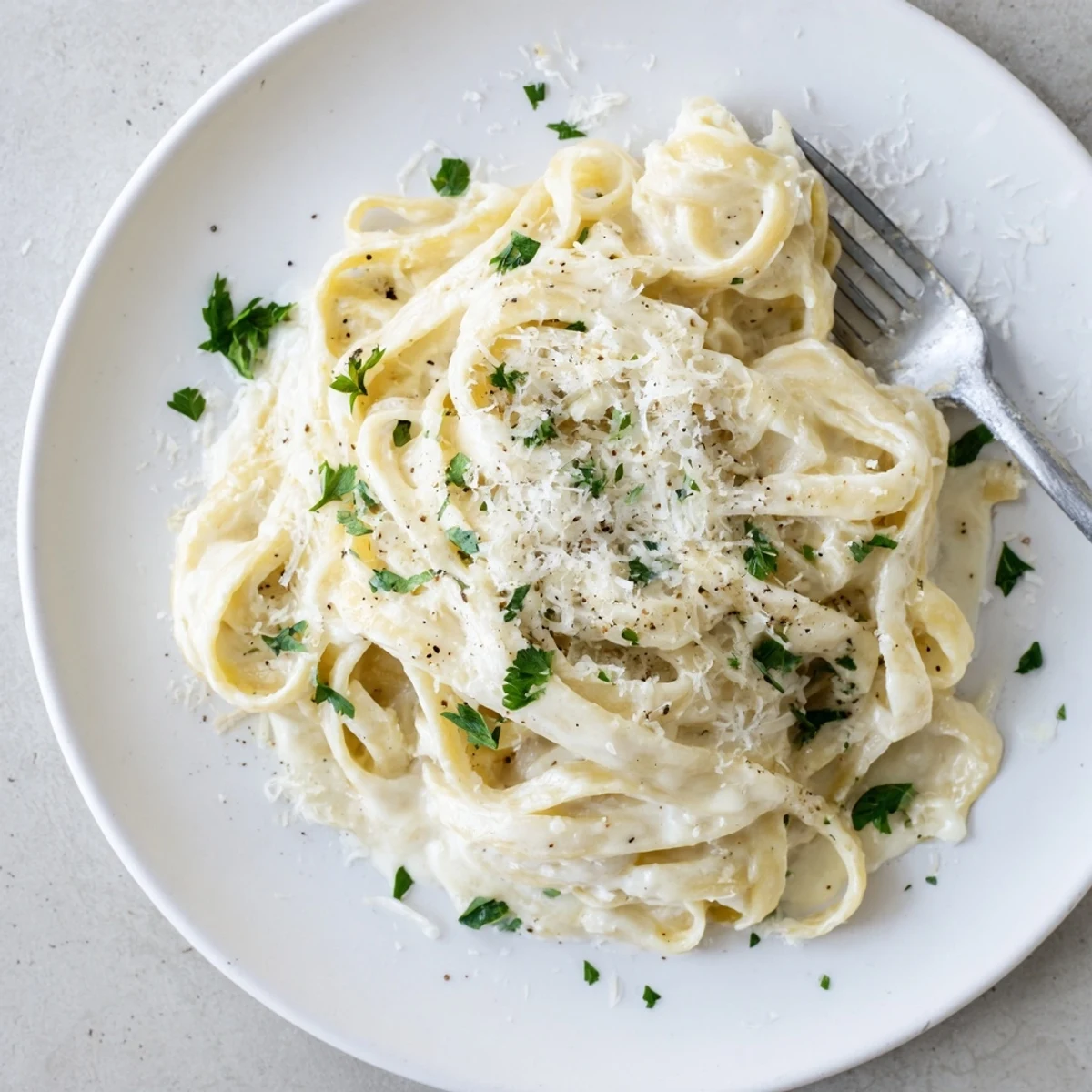 A bowl of Easy Creamy Cauliflower Alfredo pasta, coated in a velvety white sauce and garnished with fresh parsley and grated Parmesan.  