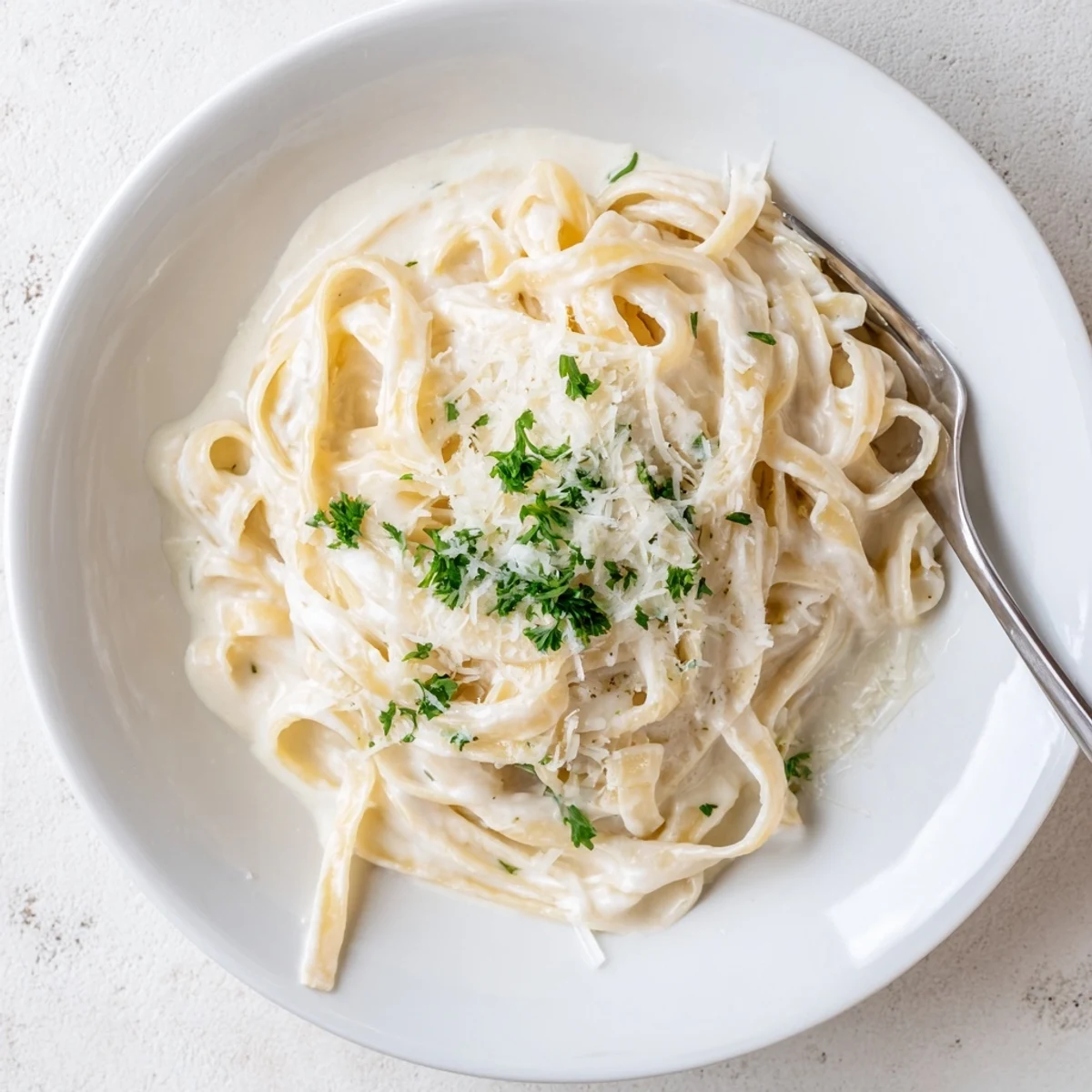 Easy Creamy Cauliflower Alfredo twirls on a fork, with a creamy cauliflower sauce clinging to golden fettuccine noodles.  