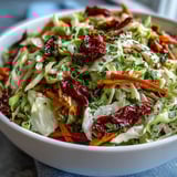 Freshly tossed Cabbage Salad With Sundried Tomatoes featuring crunchy julienned carrots, bell peppers, and scallions, glistening with olive oil and vinegar dressing on a wooden table.