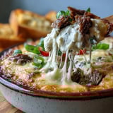 Creamy hot Philly Cheesesteak Dip baked in a dish with melted provolone and toasted bread.