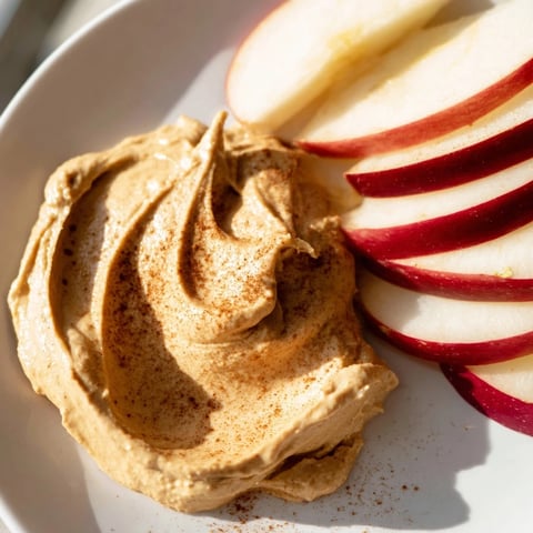 Fresh apple slices ready for dipping next to a small bowl of creamy peanut butter for snacking.
