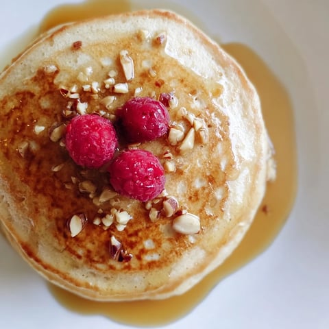 A stack of warm brown banana pancakes, golden brown and dotted with ripe banana pieces, drizzled with maple syrup.