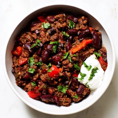 This flavorful one-pot chocolate chili features a glistening surface, with toppings of fresh cilantro and cheese.