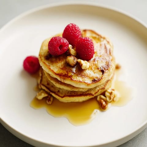 Freshly cooked brown banana pancakes on a white plate, topped with fresh berries and a dollop of Greek yogurt.