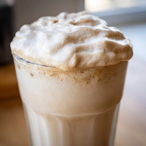 A fluffy cloud of whipped Dalgona coffee perches on steaming milk, ready to be stirred into a creamy, sweet sip.