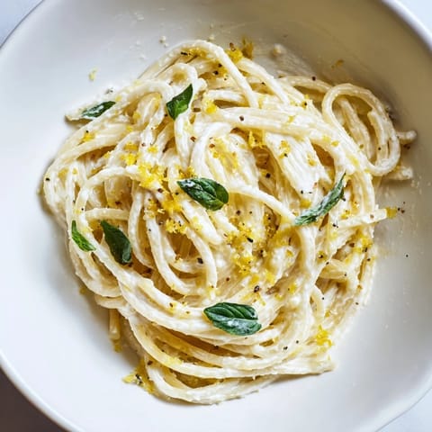 Close-up of steaming Lemon Ricotta Pasta, showcasing glossy strands of spaghetti coated in a creamy ricotta-lemon sauce on a rustic wood table.