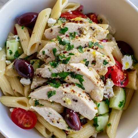 Creamy feta and crisp cucumbers garnish a vibrant Greek Chicken Pasta Bowl, finished with a drizzle of olive oil.