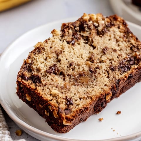 A freshly baked loaf of Chocolate Chip Peanut Butter Oatmeal Banana Bread with peanut chunks and sliced bananas on top.  