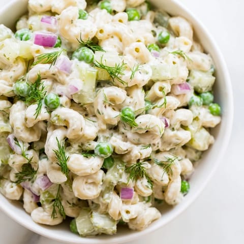 Close-up view of creamy dill pickle pasta salad, highlighting the crunchy celery, red onion, and fresh dill garnish.