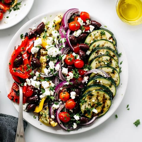 Sliced cucumbers, Kalamata olives, and a generous layer of roasted vegetables topped with a zesty lemon-oregano dressing for a warm Greek salad.