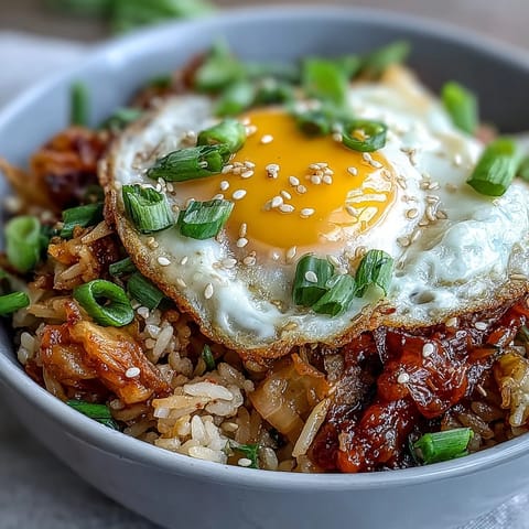 A colorful bowl of kimchi cabbage fried rice topped with a sunny-side-up egg and sesame seeds, bursting with spicy, tangy flavor.