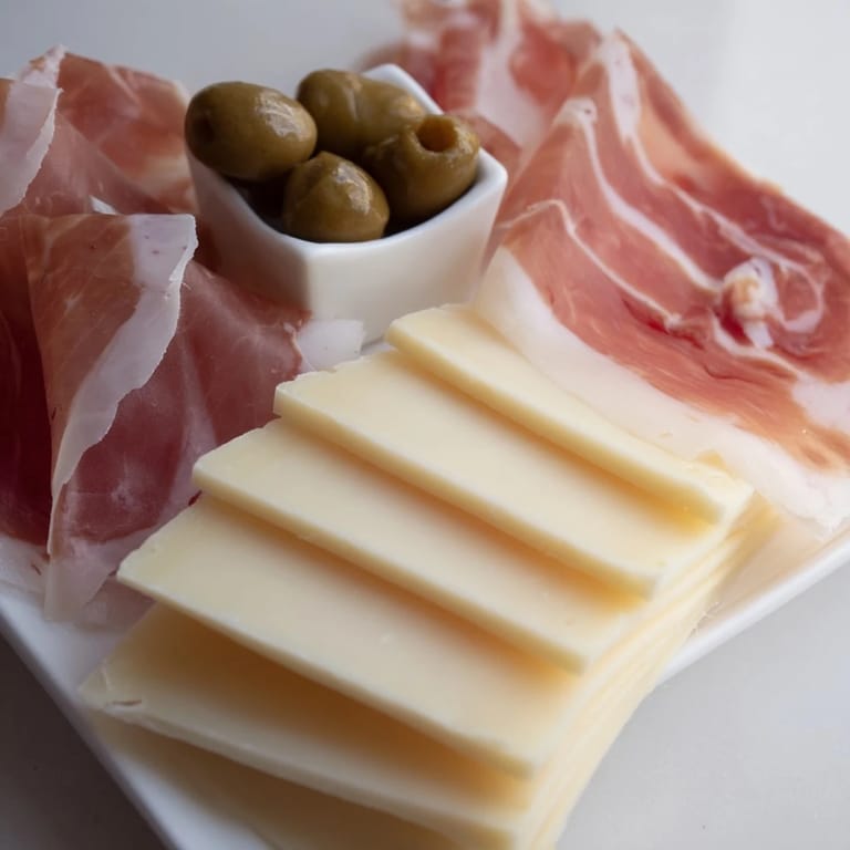 Perfectly arranged Minimalism Master showing sliced cheese, cured ham and vivid green olives, ready to serve.